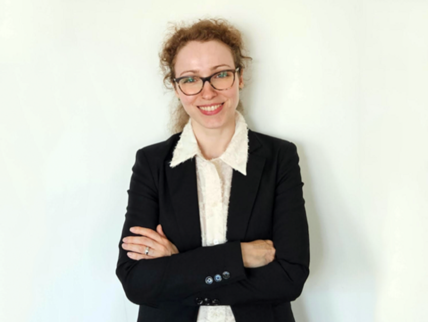 Portraitfoto einer lächelnden Akademikerin, die eine Brille und einen schwarzen Blazer trägt