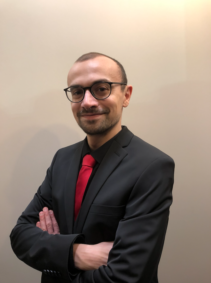 Portraitfoto eines lächelndes Mannes, der einen grauen Anzug und eine rote Krawatte trägt